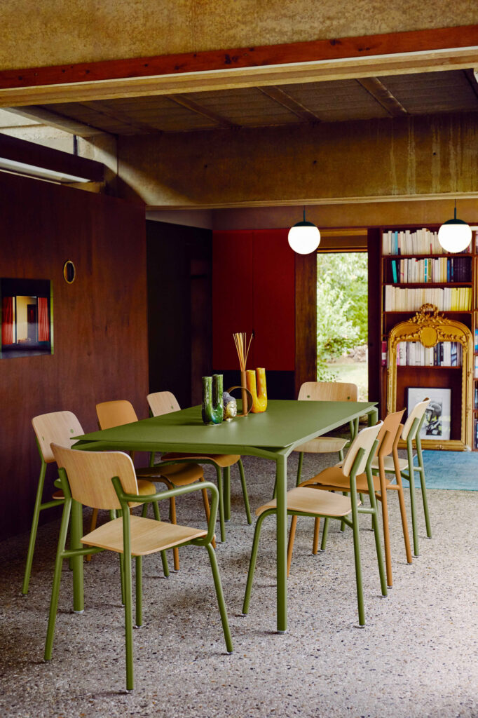 Une salle à manger moderne comprend une table verte, huit chaises Studie, des vases décoratifs, une bibliothèque, un miroir encadré d'or, des lampes suspendues et un sol en terrazzo.