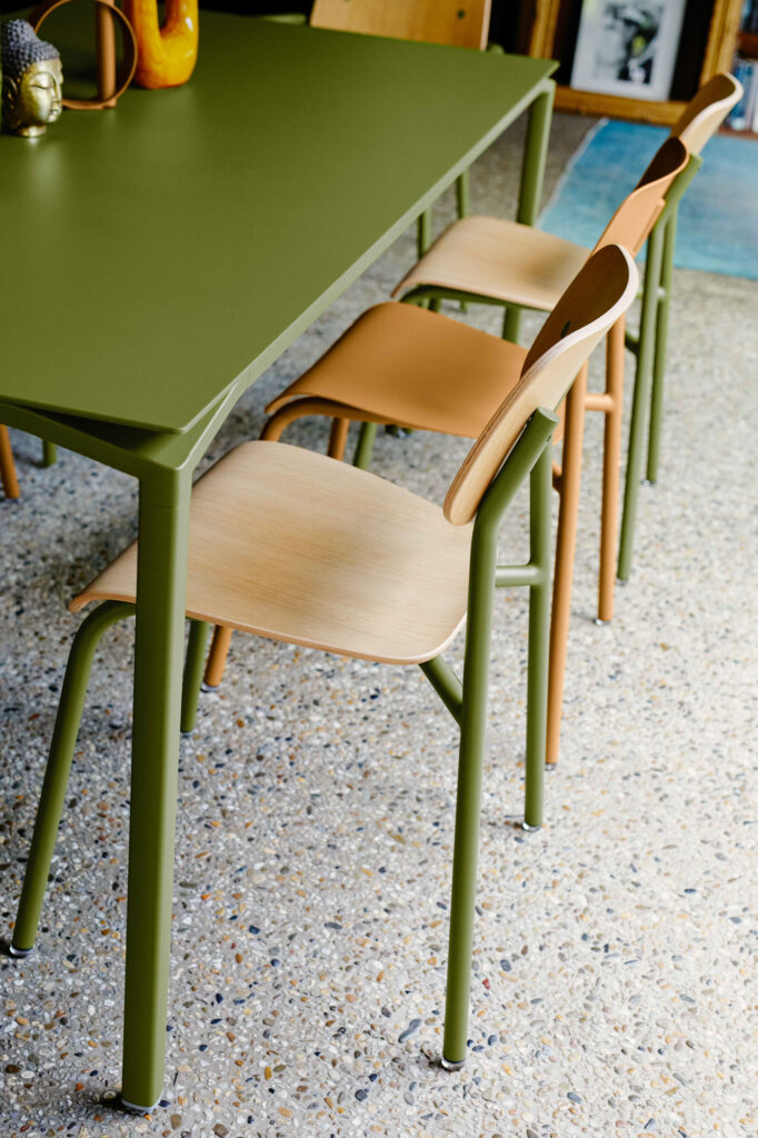 Trois chaises studieuses en bois clair entourent une table verte sur un sol moucheté dans un studio d'intérieur moderne.