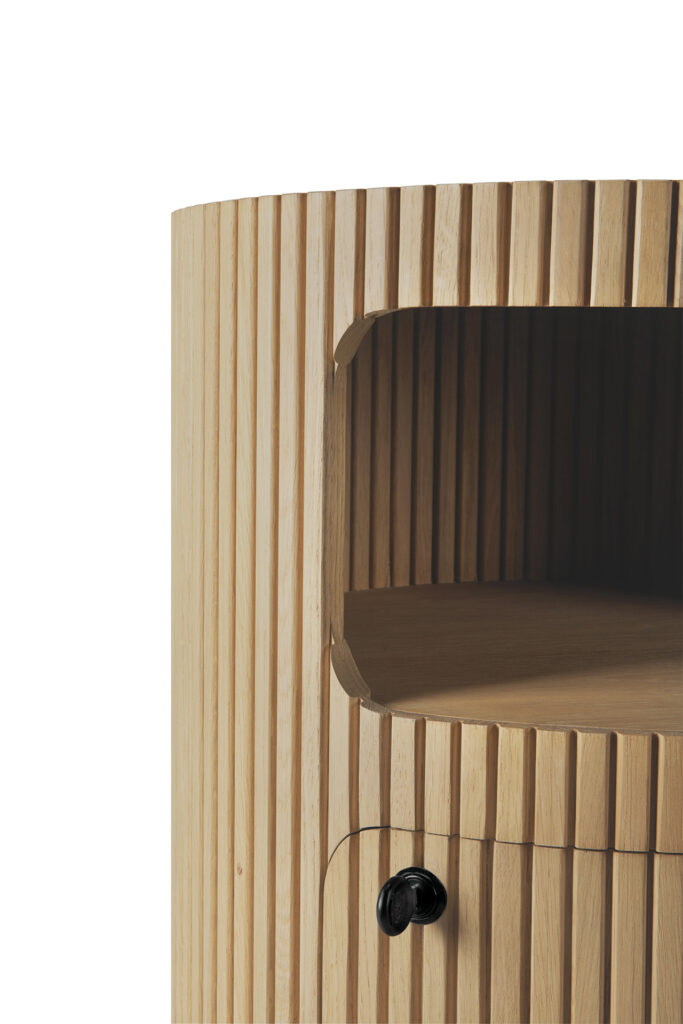 Gros plan sur un meuble Caisson Boomerang en chêne naturel huilé, avec des rainures verticales, une étagère ouverte et une poignée ronde noire sur le tiroir du dessous.