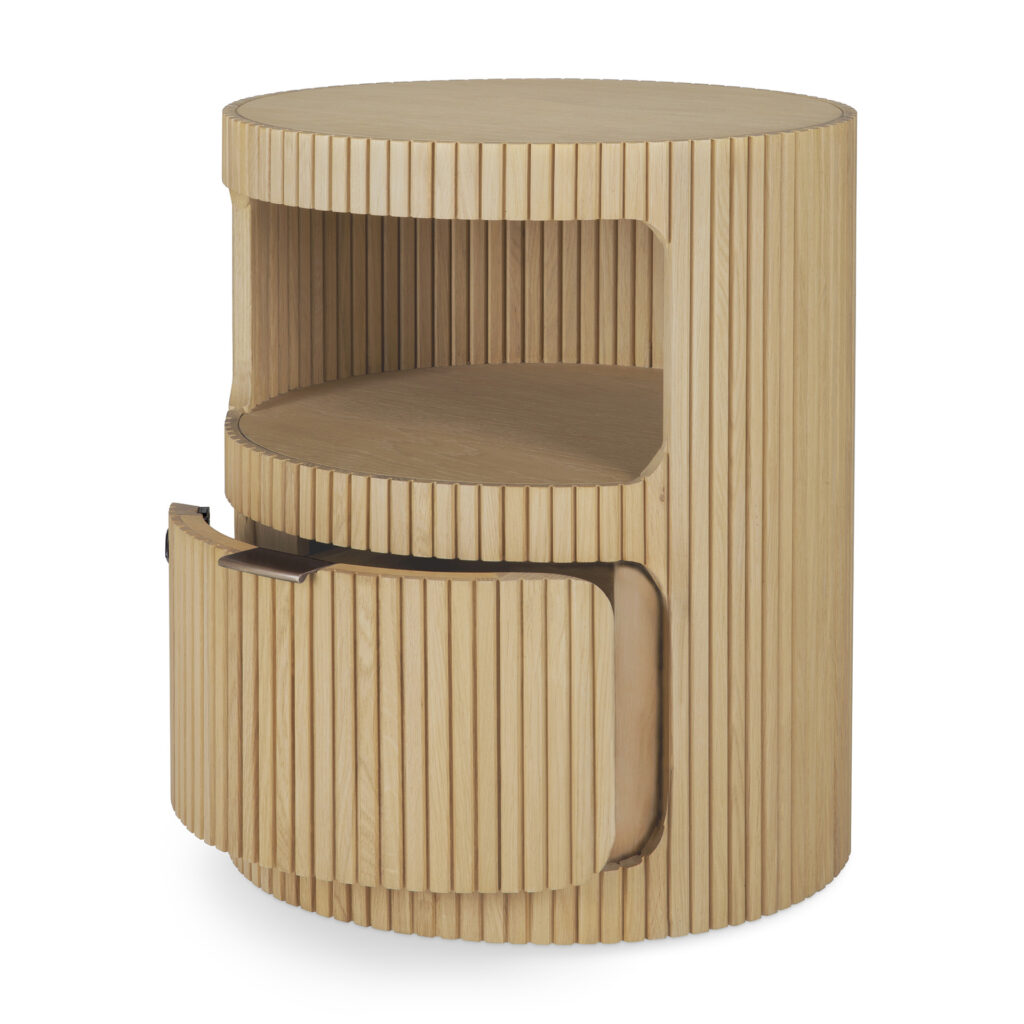 Une table de nuit ronde en chêne naturel huilé avec des rainures verticales, dotée d'une étagère ouverte et d'une porte de placard inférieure - un clin d'œil élégant au design Caisson Boomerang.