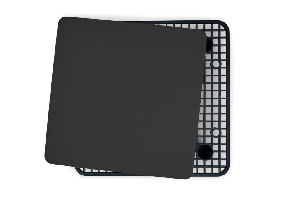 Une feuille rectangulaire noire anthracite est placée de biais sur un plateau en grille Paletti Table aux coins arrondis sur fond blanc.