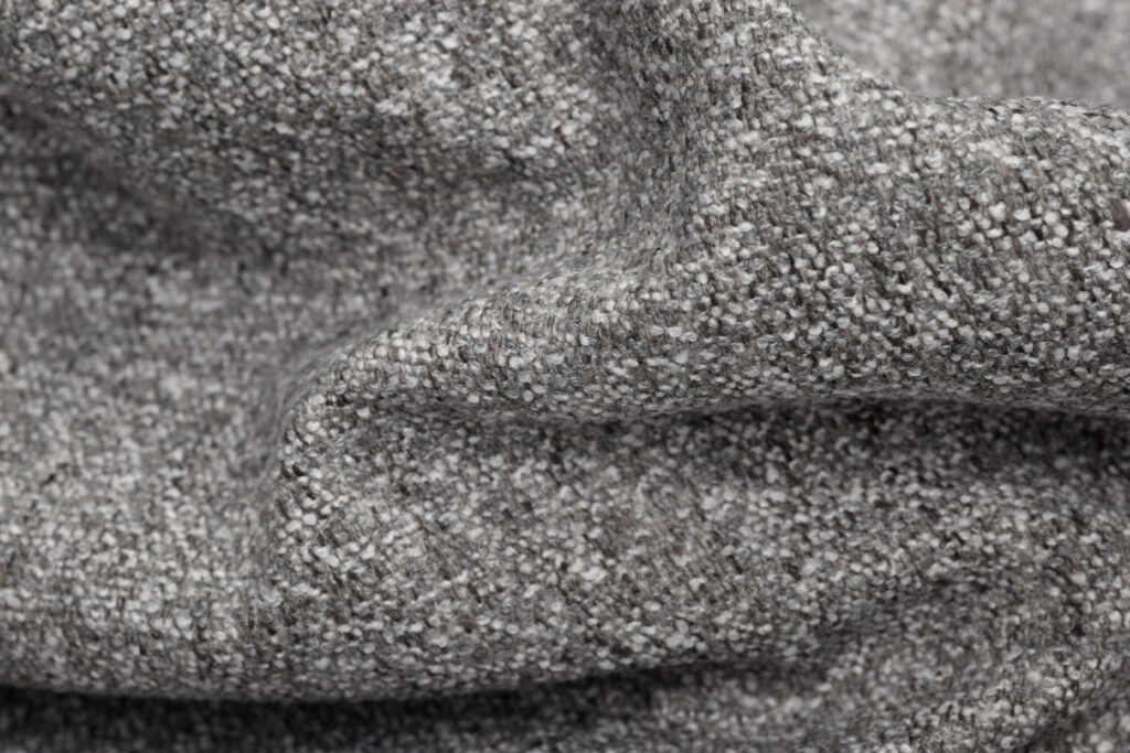 Gros plan sur un tissu gris texturé à la surface nubby et tissée, montrant les plis et les variations subtiles de couleur. Parfait pour recouvrir un Hocker ou l'associer à la collection Mingle Marble.