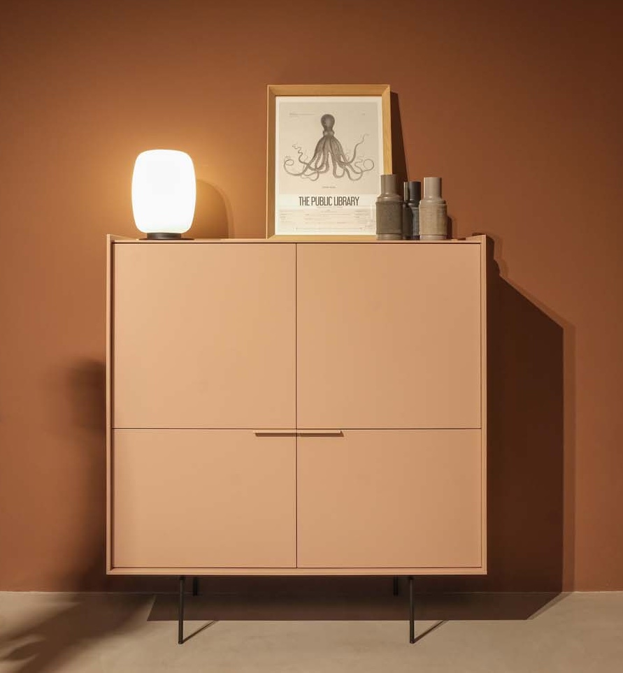 Un meuble à quatre portes de couleur pêche se dresse contre un mur brun, surmonté d'une lampe allumée, d'une pieuvre encadrée et de plusieurs objets cylindriques empilés - une configuration élégante parfaite pour mettre en valeur les trouvailles du Black Friday.