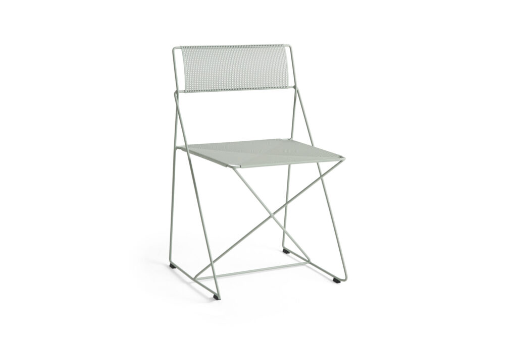 La chaise X-Line est une chaise pliante minimaliste en métal, en tilleul clair, avec un dossier perforé et une assise solide, présentée sur un fond blanc uni.