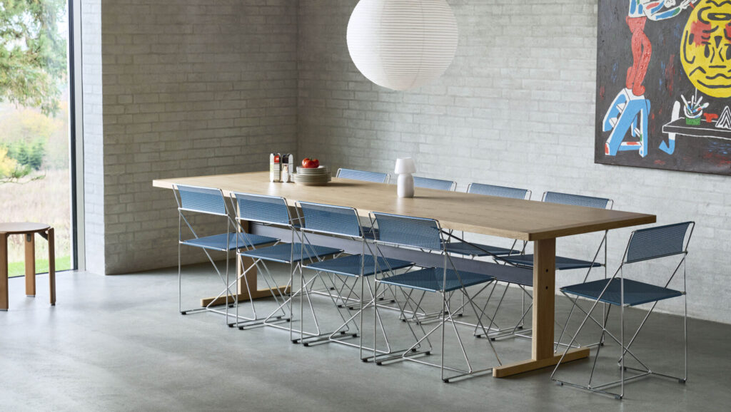 Une salle à manger moderne avec une longue table en bois, huit chaises X-Line bleues, une lampe suspendue blanche, des objets décoratifs sur la table et des œuvres d'art murales abstraites.