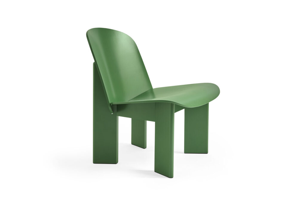 Chaise moderne d'un vert luxuriant avec une assise et un dossier incurvés, dotée de pieds larges et plats. La chaise a un design minimaliste et géométrique qui rappelle le ciseau d'un sculpteur et est photographiée sur un fond blanc.