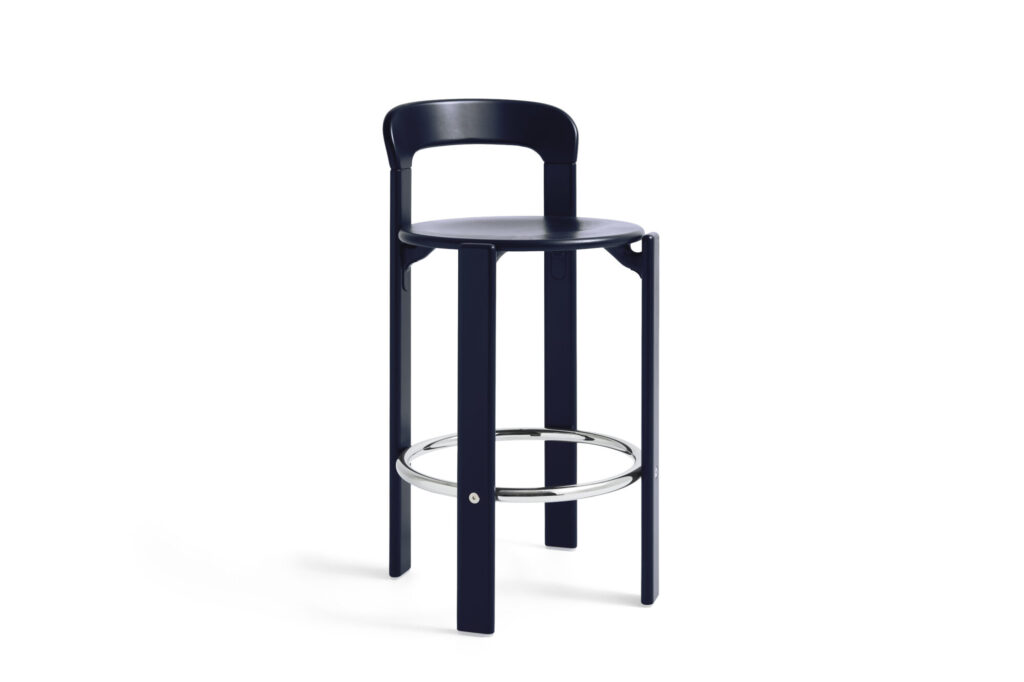 Un tabouret de bar Tabouret haut noir avec une assise ronde, un dossier bas incurvé, trois pieds droits et un repose-pieds circulaire en métal se détache sur un fond blanc. De subtils accents bleu foncé ajoutent une touche de modernité à ce design inspiré de Rey.