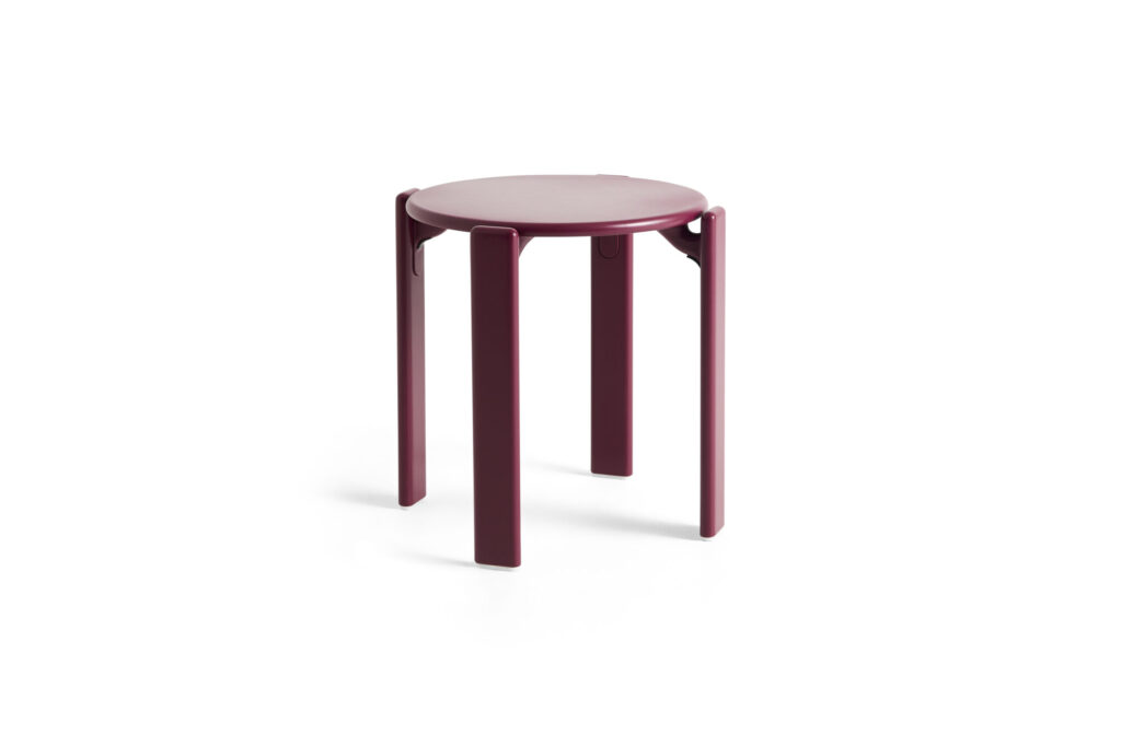 Tabouret Tabouret Rey rond et minimaliste de couleur bordeaux, avec quatre pieds droits et une assise plate, sur un fond blanc crème uni.