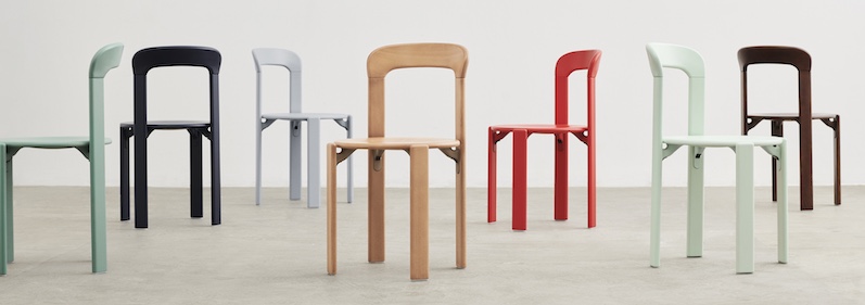 Une rangée de chaises modernes de différentes couleurs, dont le vert menthe, le noir et le bois naturel, disposées dans une pièce minimaliste avec un mur uni et un sol en béton - parfait pour tout amateur de design quatuor ou de magasin de meubles design.