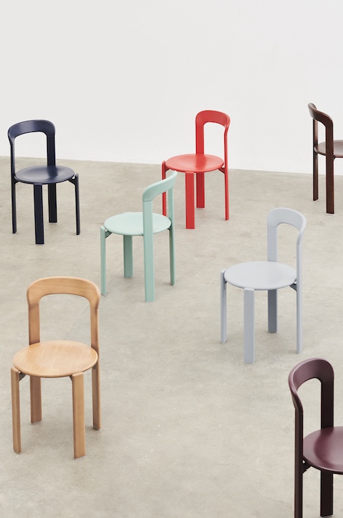 Plusieurs chaises minimalistes de style quatuor en marine, menthe, rouge, beige, marron, gris et marron sont espacées sur un sol en béton clair contre un mur blanc uni - parfait pour n'importe quel magasin de meubles design.