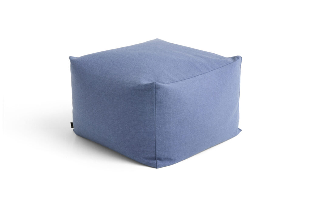 Pouf ottoman en tissu bleu en forme de cube avec des coutures visibles, placé sur un fond blanc.