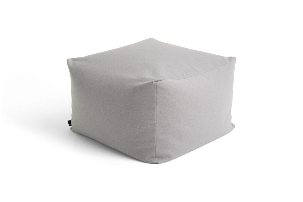 Un pouf en tissu gris clair uni aux bords doux est placé sur un fond blanc, offrant un contraste subtil qui se marie à merveille avec des accents bordeaux.