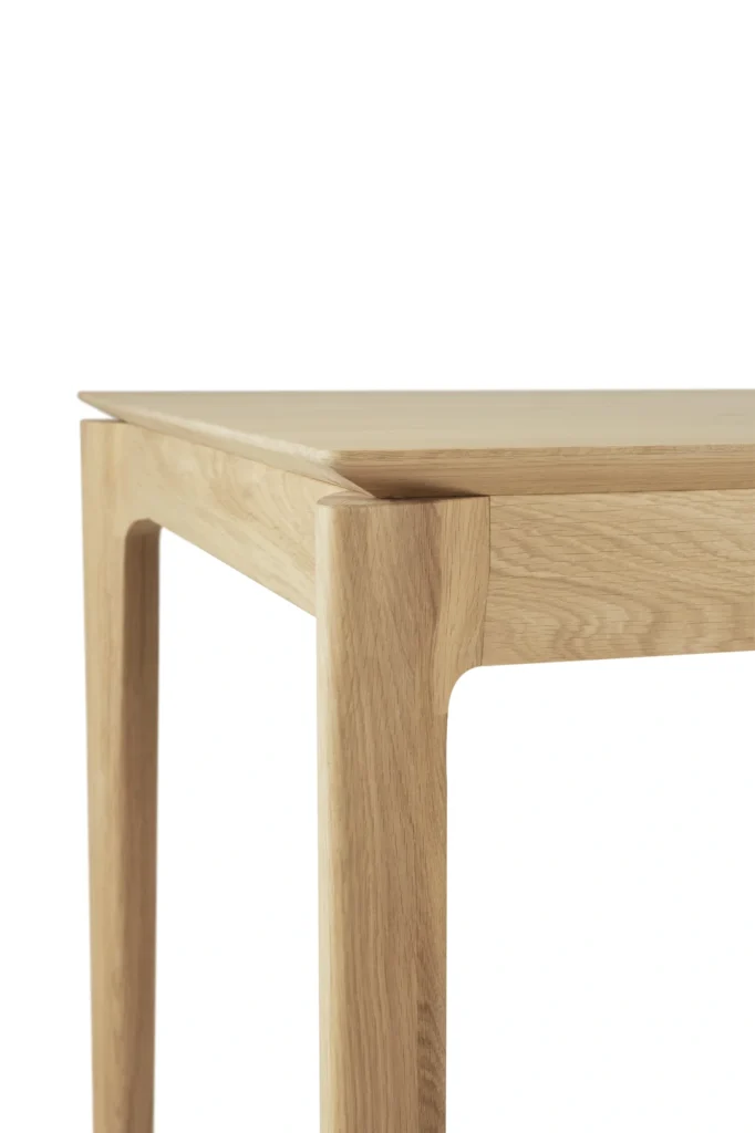 Gros plan sur une table à rallonge en chêne naturel verni, aux lignes épurées et au design minimaliste, sur fond blanc.