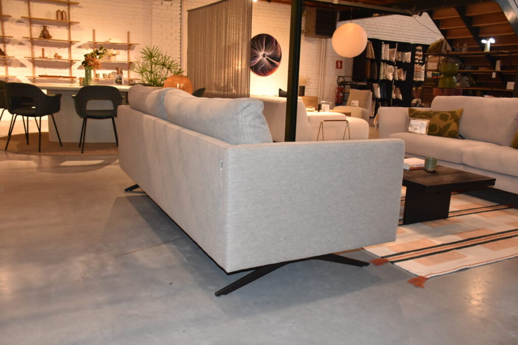 Un salon moderne présente le Canapé Diva 3 places en tissu Colourwash avec un piètement noir, complété par une table basse, un coin bar et des étagères placées contre un mur de briques.