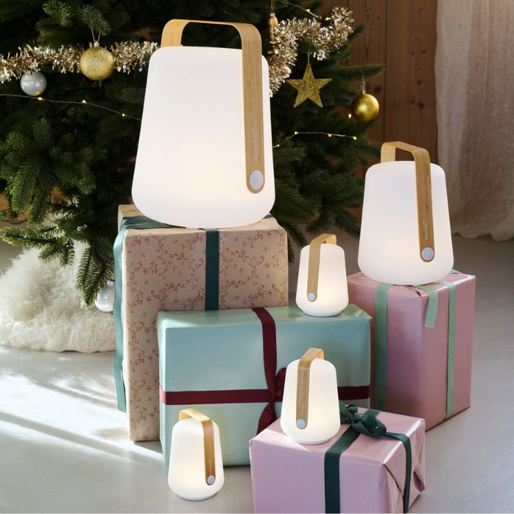 Cinq lanternes modernes avec des poignées en bois d'une collection de design quatuor sont disposées sur des cadeaux emballés de couleur pastel devant un arbre de Noël décoré.