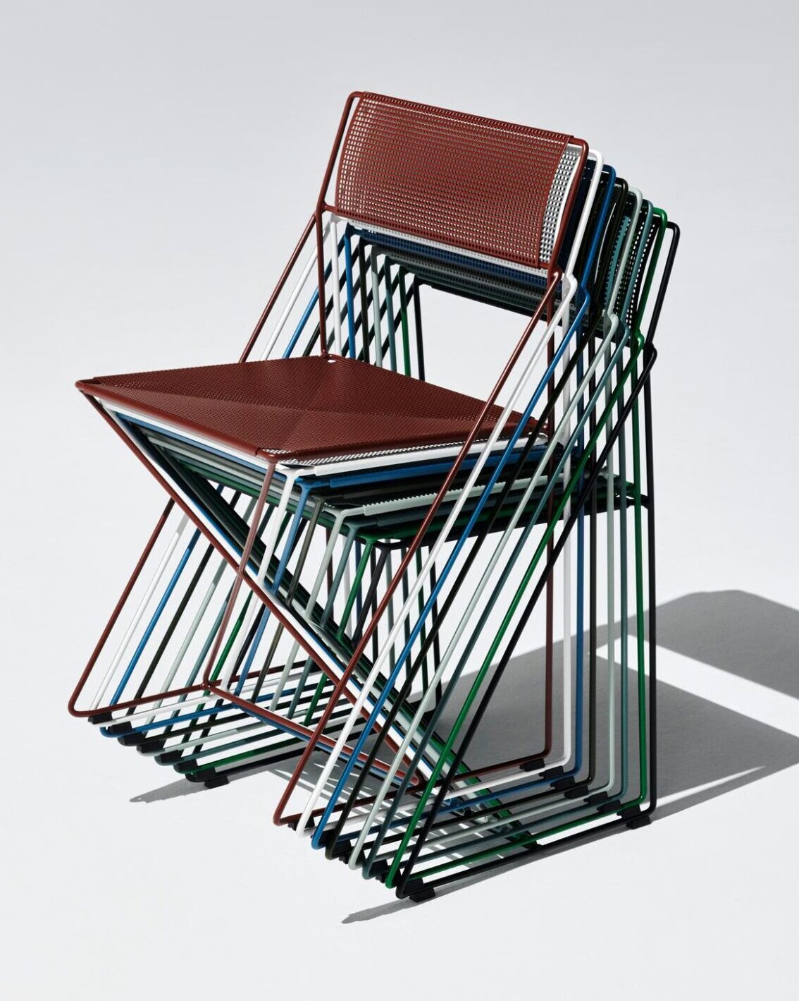 Cinq chaises modernes en métal de différentes couleurs sont empilées sur un fond clair, projetant des ombres sur la droite - un moyen idéal d'optimiser l'espace fête avec style et praticité.