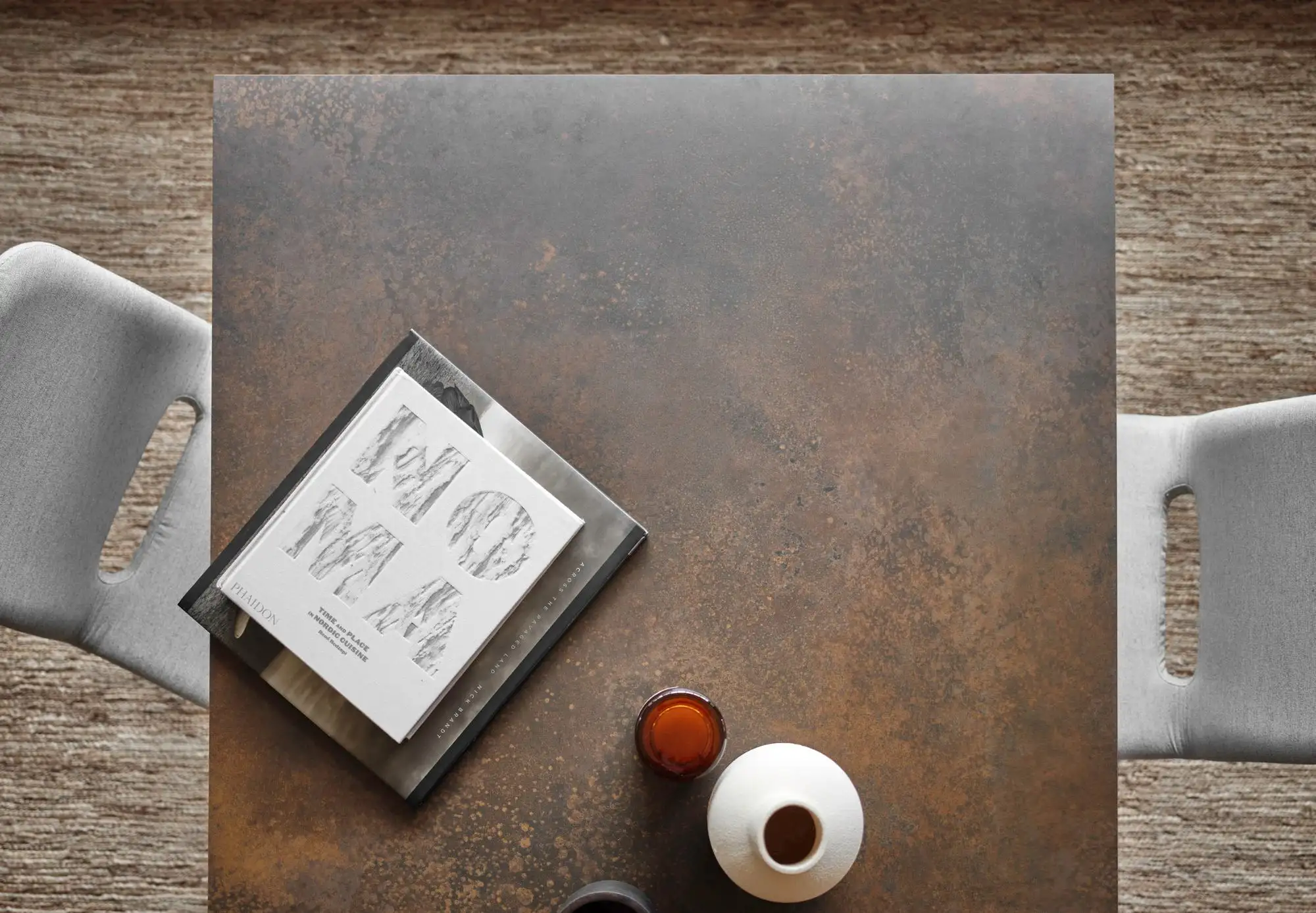 Une table en métal avec deux chaises, un livre présentant des croquis anatomiques, un plateau métallique, une petite tasse avec une boisson foncée et un vase en céramique blanche - parfait pour optimiser vos espaces pour des fêtes intimes ou des moments de détente.