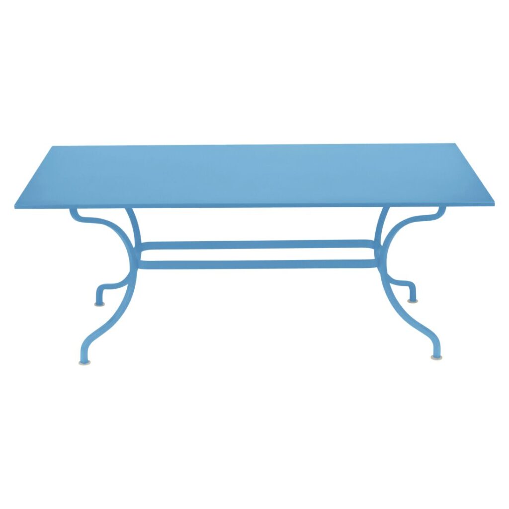 La Table Romane, en finition Bleu Maya, présente un design rectangulaire en métal bleu avec des pieds courbés et une barre de support horizontale, sur fond blanc.